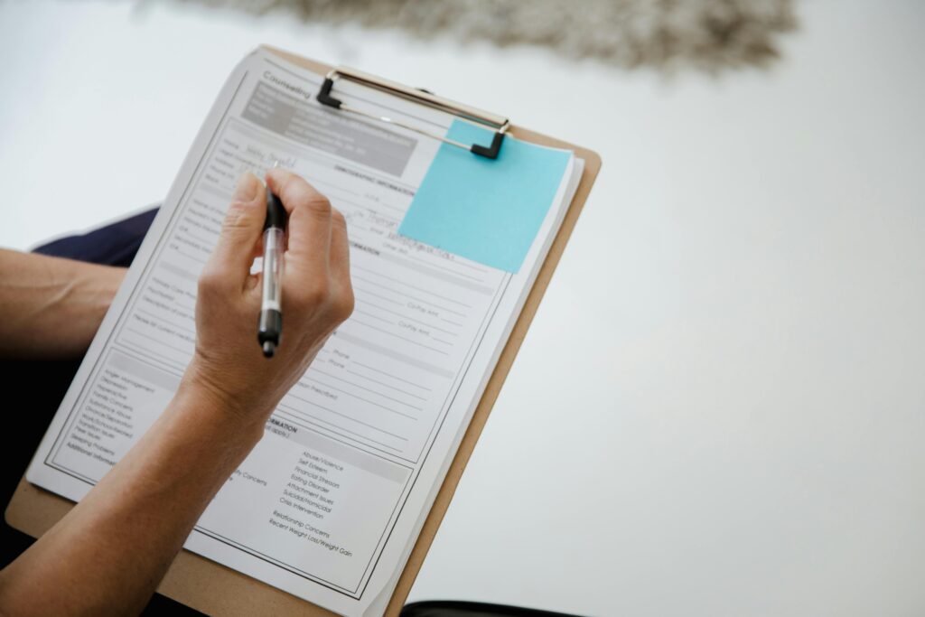 pexels-photo-9064799-9064799 A person writes on a document using a clipboard indoors.